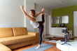 © Miljan Živković - Young caucasian woman practicing yoga at home beautiful instructor teaching online class training in apartment standing in position asana in front of camera and laptop making video in day or morning