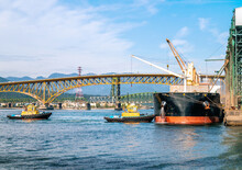 Two Tug Boats Approaching A Docked Tanker At A Port Terminal Of Vancouver. Harbour Port Panorama. Tug Boats Are Part Of The Marine Traffic Coordination Ensure Safe Movement Of Goods. 