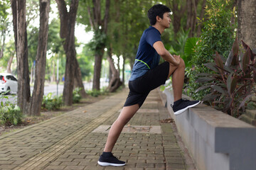 asian young fitness man runner do a strething leg before running at the park