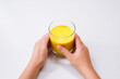 Hands holding glass of golden milk turmeric curcumin latte yellow drink on white table background with copy space