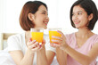 © cocorattanakorn - Asian young sisters lovely couple on white bed and smiling with hand holding Orange juice glass in bedroom.  Holiday and healthy concept. Closed up on Orange juice glass.