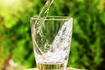 Wall Mural - Pouring drinking water into glass on blurred green nature background