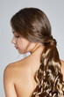 © RedUmbrella&Donkey - Cropped shot of a brown-haired lady with a wiglet made as a long chestnut ponytail with lustrous strands. The lady with naked shoulders is facing profile on the gray backdrop.