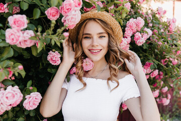 Glad blue-eyed girl posing on nature background and smiling to camera. Stunning female model in trendy straw hat relaxing flower flavour.