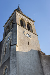 Medieval tower with clock on sunny morning. Facade of ancient church in morning sunlight in France. Religious architecture concept. Travel in Europe. 