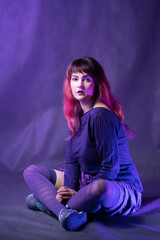 Wall Mural - Beautiful girl in studio portrait in violet-blue image. Portrait of young woman in creative image posing sitting in striped stockings