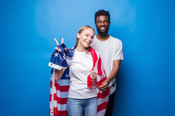 African man and caucasian woman covered with american flag isolated on blue background. Unity of american people.