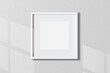 © Idol Design - Minimal empty square white frame picture mock up hanging on white wall background with window light and shadow. isolate image
