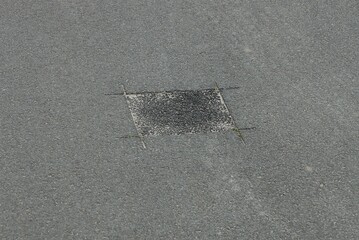 square black pothole patch on the gray asphalt of a repaired road