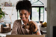 © Prins Productions - Beautiful mixed race woman working from home on her laptop with dog on her lap