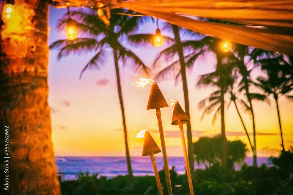 Hawaii luau party with fire torches at sunset. Hawaiian icon, lights burning at dusk at Waikiki beach resort restaurant for outdoor lighting cozy atmosphere. - obrazy, fototapety, plakaty 