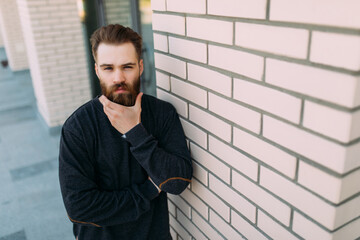 Portrait of a brutal bearded man walking in the street. Young stylish hipster possing near brick wall