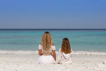 Wall Mural - Young beautiful mother with her charming daughter in white clothes walk on a sandy beach near the water