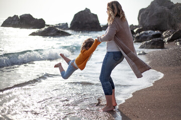 Family posing outdoor in the beach of the sea at spring time. woman with daughter have fun on vacation near ocean. Female parent holds childs hand and circling. 