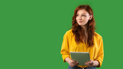 Millennial Girl Holding Tablet Computer Looking Aside On Green Background