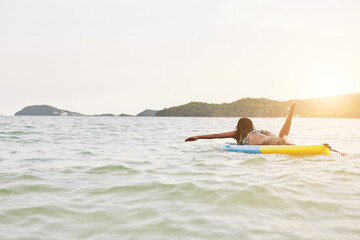 Wall Mural - Black young woman swimming on sup board in the ocean in rayS of declining sun