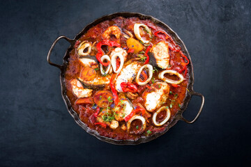 Wall Mural - Traditional Brazilian fish stew moqueca capixaba with fish filet and squid rings in tomato sauce as top view in a rustic pan