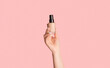 Cropped view of millennial girl showing bottle of makeup foundation on pink background