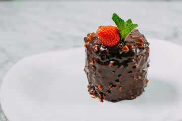 chocolate cake with nuts, strawberries and mint in a white plate on a marble table