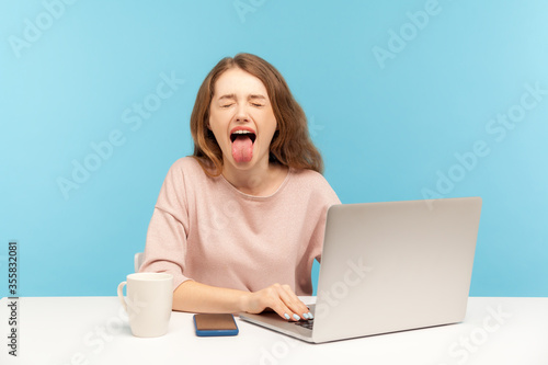 Naughty overworked businesswoman in casual clothes showing tongue out, expressing disgust and disobedience while working on laptop at home office Tableau sur Toile