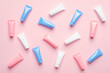 Many colorful cosmetic tubes on pink background. Blank plastic beauty products packaging. Flat lay, top view.