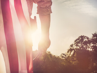 Young engineer, white hardhat and an American Flag in the park against the backdrop of green trees and the setting sun, looking into the distance. Close-up. Concept of labor and employment