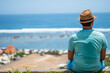 © Souvik - A tourist sitting on a cliff and enjoying a hot summer day wearing colourful dress and round hat beside a sea beach in Bali