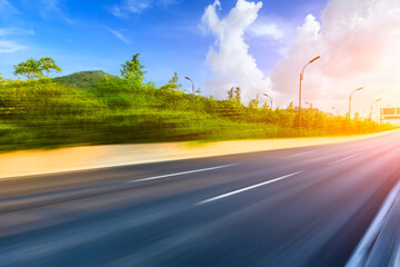 Motion blurred asphalt road and green mountain landscape at sunset.