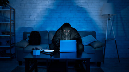 Fototapete - Masked hacker downloading private information using laptop