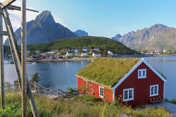 Petite maison rouge au toit d'herbe au bord de l'eau dans une baie des îles Lofoten avec village