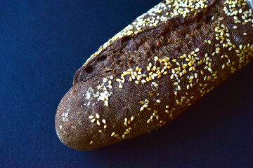 A loaf of black bread with sesame seeds on a black background