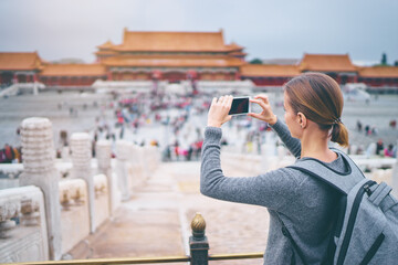 Wall Mural - Enjoying vacation in China. Travel and technology. Young woman with smartphone taking photo at Forbidden City, Beijing.