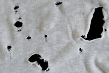 Gray White Fabric With Many Holes. Texture Of An Old Dirty Ragged T Shirt. Grunge Damaged Cloth On Black Background. Copy Space