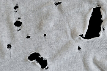 Gray white fabric with many holes. Texture of an old dirty ragged t shirt. Grunge damaged cloth on black background. Copy space