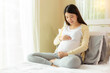 © Nutlegal - Happy pregnant young asian woman touching belly and admiring her baby or fetus on bed with happiness smile face. Young Asia mother love her baby so much. Mom waiting and expecting baby has good health