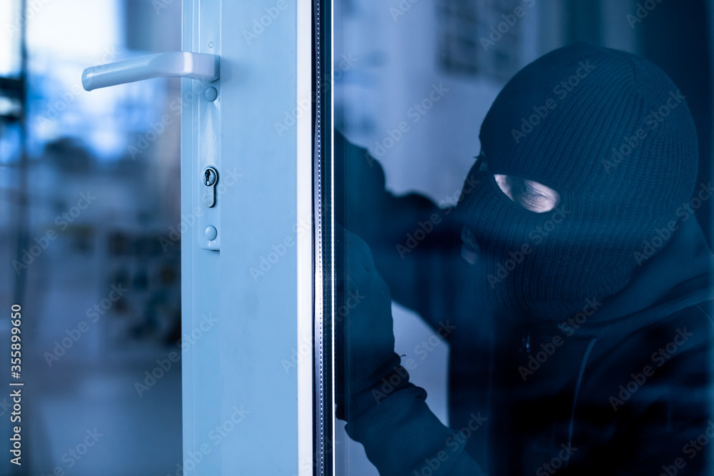 Robber in black balaclava cracking door with metal picklock - obrazy, fototapety, plakaty 