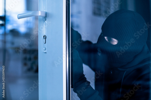Cuadros en Lienzo Robber in black balaclava cracking door with metal picklock