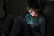 Young boy using smartphones sittingon a sofa at home, entertaining online obsessed with modern devices, gadget addiction