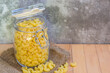 Close-up of Uncooked Macaroni in a glass jar placed on the wooden table with cement wall background , selective focus.