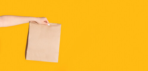 Wall Mural - Millennial woman holding paper bag with takeaway food on orange background, empty space