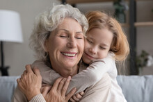 Cute Caring Small Granddaughter Embrace Cuddle Smiling Middle-aged 60s Grandmother, Relax Together At Home, Little Grandchild Hug Senior Grandparent, Show Love And Gratitude, Family Unity Concept