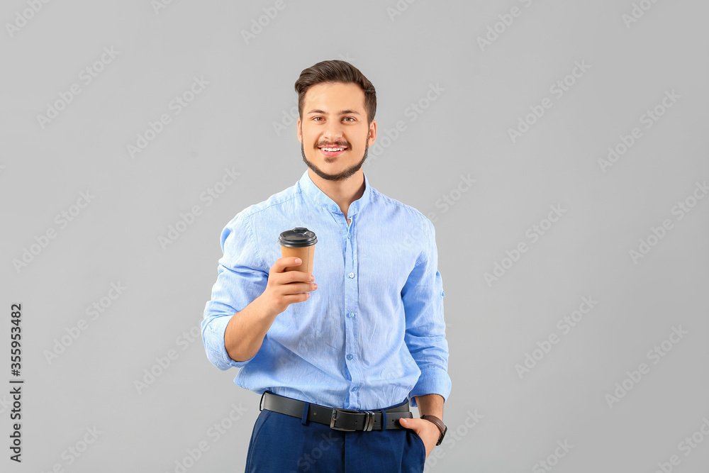 Handsome young businessman with coffee on grey background