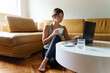 © Miljan Živković - Young adult caucasian woman working on the laptop computer from home sitting on the sofa bed in day taping online female freelancer or shopping online efficiency and expertise making money concept