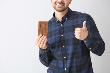 Sticker - Handsome young man with tasty chocolate showing thumb-up on light background