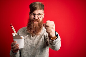 Redhead Irish man with beard holding box of ramen eating asian food using chopsticks annoyed and frustrated shouting with anger, crazy and yelling with raised hand, anger concept