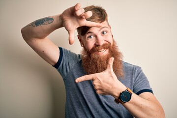 Poster - Handsome Irish redhead man with beard and arm tattoo standing over isolated background smiling making frame with hands and fingers with happy face. Creativity and photography concept.