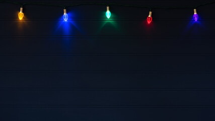 Christmas Lights on String Glowing against a Dark Navy Blue Wood Board Background with Copy Space below with a horizontal crop