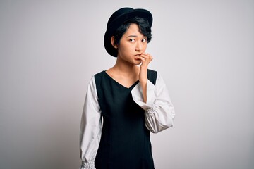 Poster - Young beautiful asian girl wearing casual dress and hat standing over isolated white background looking stressed and nervous with hands on mouth biting nails. Anxiety problem.