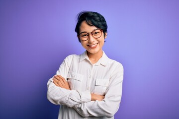 Wall Mural - Young beautiful asian girl wearing casual shirt and glasses standing over purple background happy face smiling with crossed arms looking at the camera. Positive person.