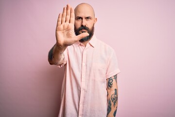 Poster - Handsome bald man with beard and tattoo wearing casual shirt over isolated pink background doing stop sing with palm of the hand. Warning expression with negative and serious gesture on the face.